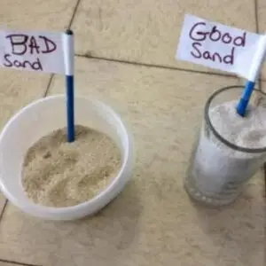 Two cups of sand on a table labeled 'Bad Sand' and 'Good Sand', illustrating a contrast in sand quality (left is poor, right is better).